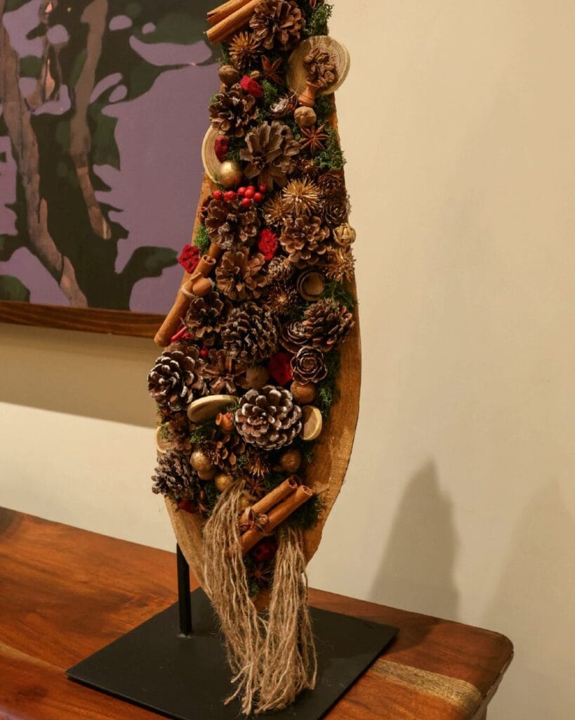 Vertical bark piece with pine cones, cinnamon and dried fruit on a metal stand.